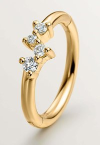 Anillo de oro que presenta tres piedras preciosas transparentes, de corte redondo, engastadas en garras elevadas, con una banda lisa y un acabado pulido.