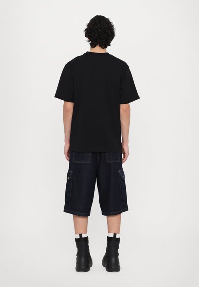 T-shirt noir à manches courtes associé à un short cargo en denim foncé avec des poches latérales, sur un fond blanc uni.