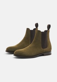 Botas de tobillo de ante oliva con paneles elásticos oscuros a los lados, punta redondeada, bucles para tirar y una suela de cuero marrón lisa.