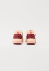 Rear view of sneakers featuring a maroon leather upper, soft pink textile tongue, and light beige rubber sole with textured detailing.
