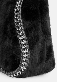 Schwarze Handtasche aus Kunstfell mit einem geflochtenen Riemen und metallischen Verbindungen sowie einer strukturierten Oberfläche. Enthält ein kleines Markenschild.