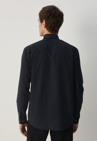 Marineblaues Hemd mit Knöpfen und dezentem Punktmuster, langen Ärmeln und klassischem Kragen, aus leichtem Stoff gefertigt. Flacher Rücken mit taillierter Passform.