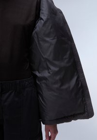 Sort oversized pufferjakke med brede ærmer, tekstureret stof og quiltet finish, parret med sorte bukser med elastisk talje.