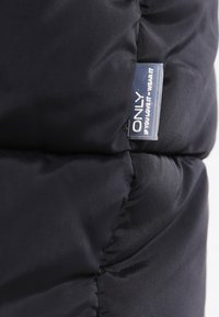 Primer plano de una tela de tiro negro con una pequeña etiqueta rectangular que dice "SOLO SI TE ENCANTA - LÚCELO" cosida en la costura.