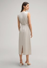 Mouwloze beige midi-jurk met een ceintuur in de taille, een ritssluiting aan de achterkant en een zijsplit. Gemaakt van een gladde stof met een subtiele glans.