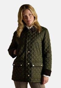 Pikowana zielona kurtka z brązowym kołnierzem, dwoma przednimi kieszeniami i zapięciem na napy. Posiada diamentowy wzór na teksturowanej tkaninie.