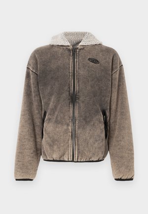 Jachetă maro cu fermoar din fleece, cu glugă căptușită cu sherpa și buzunare laterale, având un mic patch negru cu logo pe partea stângă a pieptului.