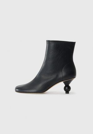 Bota de couro preta até o tornozelo com bico pontudo e um salto arredondado em forma de bola. Textura suave com um contorno elegante.