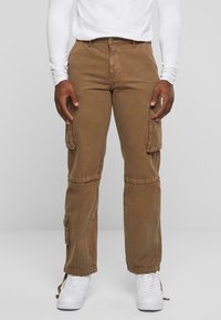 Pantalons cargo bruns avec poches latérales, en tissu doux. Design à jambe droite et poignets ajustables. Portés avec des baskets blanches.