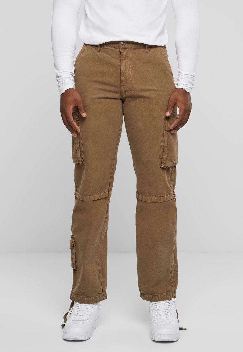 Pantalons cargo bruns avec poches latérales, en tissu doux. Design à jambe droite et poignets ajustables. Portés avec des baskets blanches.