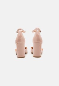 Pink patent leather high-heeled shoes with an ankle strap, rounded toe, and chunky heel. Smooth surface with a glossy finish.