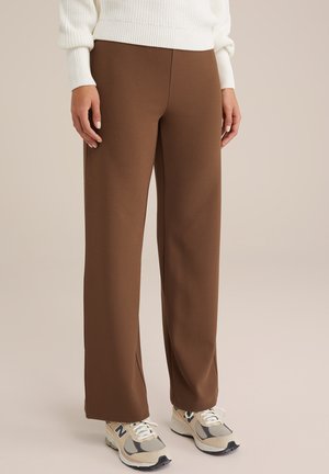 Pantalones anchos marrones fabricados con un tejido suave, que presentan un diseño limpio. Combinados con zapatillas beige y grises para un contraste.