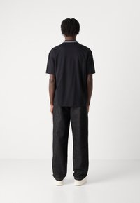 Zwarte polo met korte mouwen en een contrasterende kraag, gecombineerd met loszittende donkere denim jeans en lichtgekleurde sneakers.