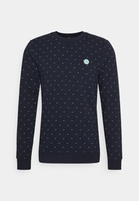 Sudadera azul marina con escote en V, que presenta un patrón de pequeños motivos en tonos verde azulado y un parche de logo verde en el pecho. Puños y dobladillo acanalados.