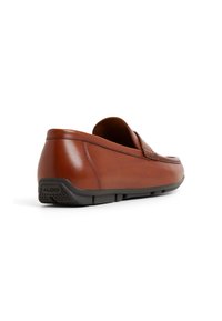 Mocasín de cuero marrón con un diseño elegante, punta redondeada y acentos texturizados. Suela de goma negra con un patrón de agarre triangular.