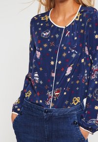 Blusa navy con una stampa colorata e fantasiosa che include stelle e navi; presenta un colletto bianco bordato e maniche lunghe.