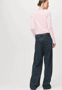 Roza majica z dolgimi rokavi je kombinirana z ohlapnimi temno modrimi kavbojkami. Hlače imajo visok pas in več zadnjih žepov.