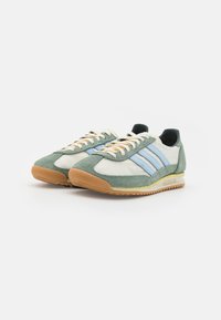 Grønn og hvit sneakers laget av semsket skinn og syntetiske materialer, med lys blå striper, beige snører og såle av gummi.