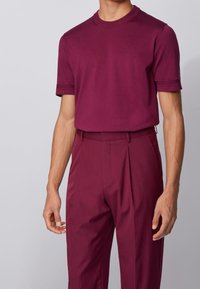 Maglietta a maniche corte bordeaux con scollo rotondo abbinata a pantaloni sartoriali coordinati, dotati di pince e una texture liscia.