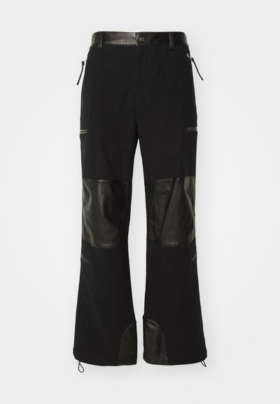 Schwarze Hosen aus einer Mischung aus Stoff und Leder, mit Lederpaneelen an den Knien, verstellbarem Bund und mit Reißverschlüssen versehenen Taschen.