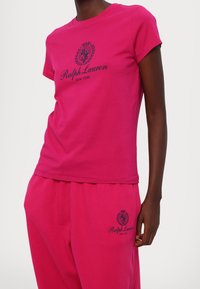 Henkilö, jolla on päällään kirkkaan pinkki Ralph Lauren -t-paita ja siihen sopivat housut, joissa on musta logo ja vaakuna rinnassa ja reisissä.