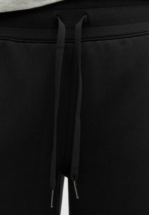 Black sweatpants with a textured finish, featuring a drawstring waist and silver metal tips on the drawstrings.