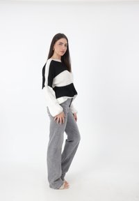 Maglione lavorato a maglia a righe bianche e nere con una vestibilità comoda, abbinato a jeans grigi chiari, in piedi su uno sfondo bianco.