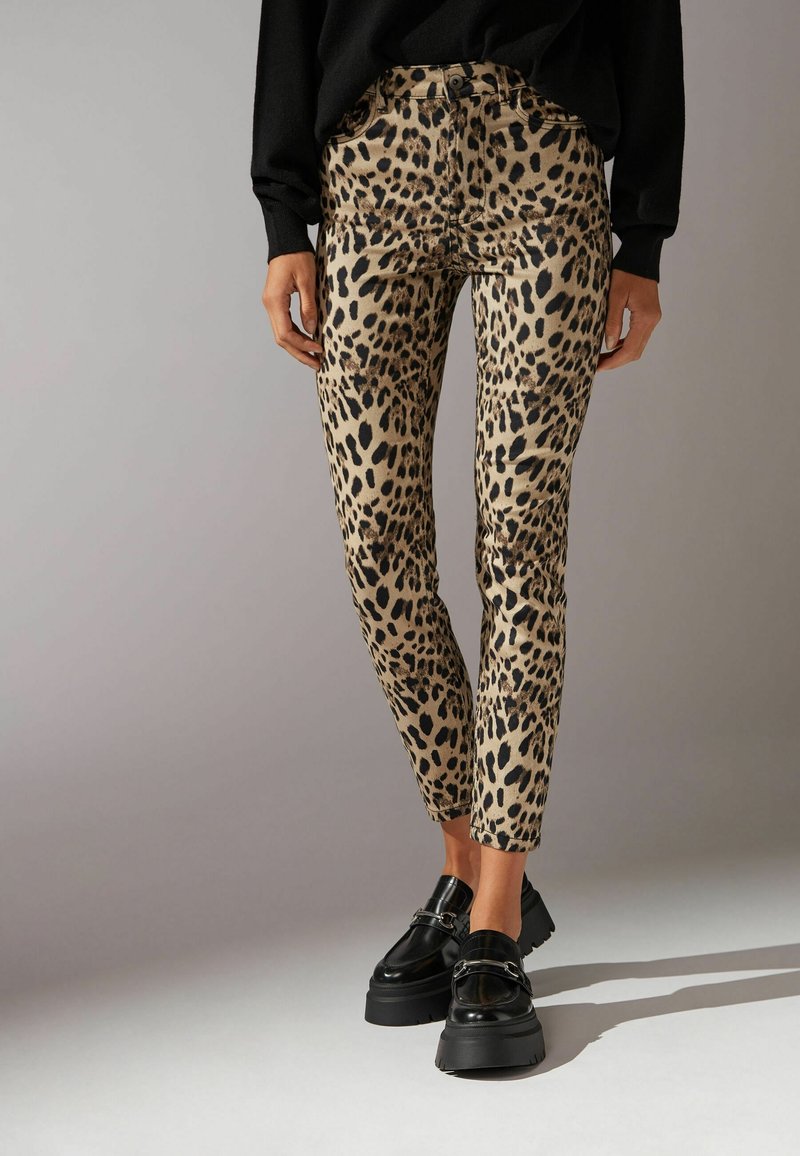 Pantaloni a stampa leopardo in beige e nero, con una vestibilità slim, vita alta, cinque tasche e chiusura con bottone. Indossati con scarpe nere chunky.