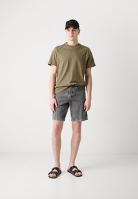 T-shirt vert olive, short en denim gris, casquette noire et sandales à glissière marron. Tenue décontractée avec une coupe relax et des textures de tissu standards.
