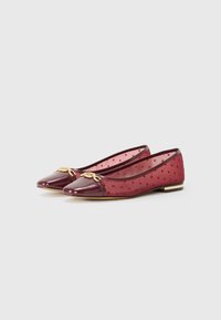 Burgundy ballet flats made of patent leather with sheer polka dot mesh. Features a rounded toe and gold-tone hardware accent on the vamp.