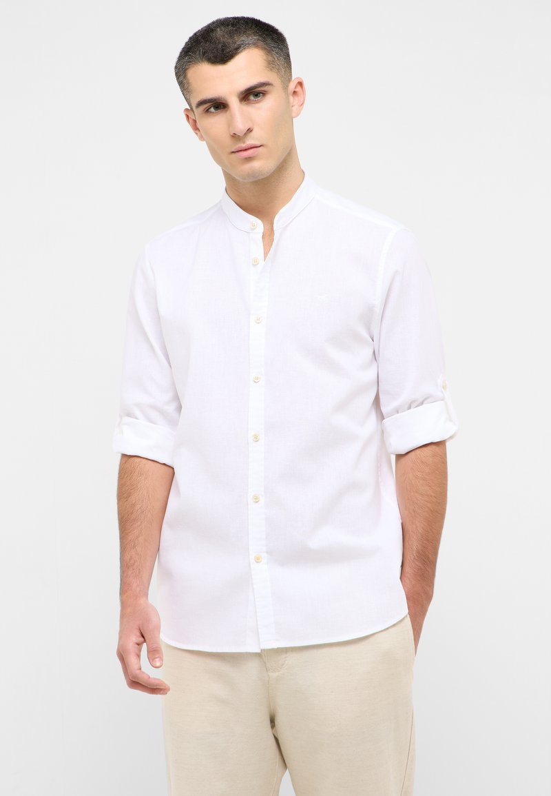 Camicia bianca a maniche lunghe con colletto alla cinese, caratterizzata da una chiusura con bottoni e maniche arrotolate. Realizzata in un tessuto leggero.