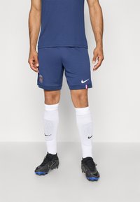 Shorts d'athlétisme navy avec un logo du Paris Saint-Germain, associés à des chaussettes blanches et des crampons Nike noirs, avec une tige texturée et des accents bleus.