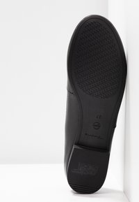 Semelle d'une chaussure noire présentant un motif antidérapant texturé et un talon marqué "ANTI SLIDE" et taille "37" sur fond blanc.
