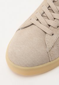 Beige semsket sneakers med rund tå, teksturert overflate, sydd detaljer og beige snøring. Gummisåle med subtilt grep mønster.