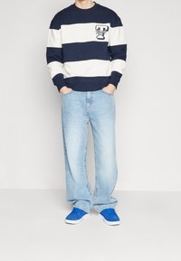 Felpa a righe navy e bianche con logo, jeans larghi azzurri e sneakers blu. Tessuto morbido con polsini e vita a coste.