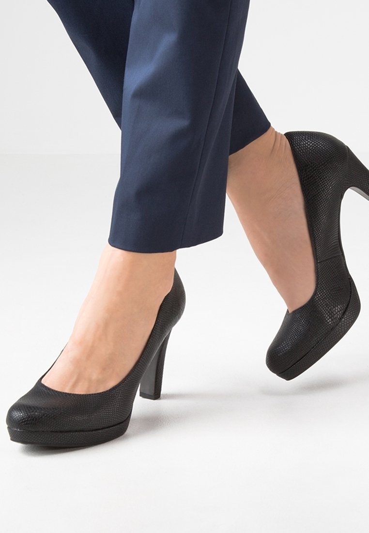 Zapatos de tacón altos negros con un acabado texturizado, puntera redonda y suela de plataforma. Los tacones son elegantes y tienen un aspecto brillante.