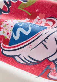 Színes textilnyomat egy kék tetejű desszerttel, piros háttérrel és dekoratív elemekkel, mint cseresznye és szívek. Texturált dizájn.