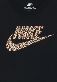 Juodas marškinėliai su dideliu Nike logotipu oranžinės ir juodos leopardų rašto dizainu. Audinys yra lygios tekstūros; apvalus kaklo iškirpimas.