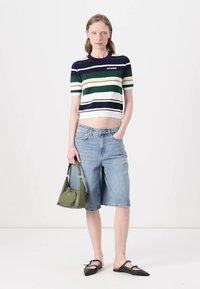 Top a maniche corte a righe blu navy, verde e bianco, abbinato a bermuda di jeans azzurri. Gli accessori includono una borsa verde e ballerine nere.