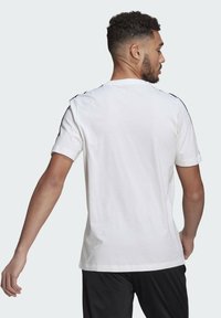 Witte t-shirt met korte mouwen en een ronde hals, voorzien van zwarte accenten langs de schoudernaden. Zachte, lichtgewicht katoenen stof.
