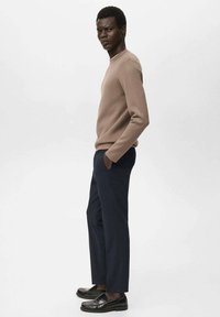 Un pull marron avec un col rond, associé à un pantalon bleu marine et des mocassins noirs. Le tissu semble lisse avec une silhouette cintrée.
