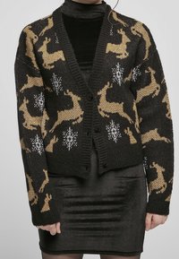 Cardigan en tricot noir avec des motifs de cerfs dorés et des flocons de neige blancs. Il a un col en V, des boutons et des manches texturées.