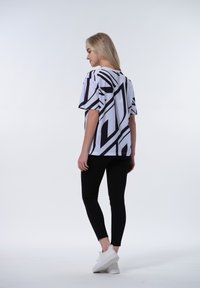T-shirt bianco con audaci motivi geometrici neri, maniche corte, abbinato a leggings neri e sneakers bianche. Tessuto liscio e vestibilità rilassata.