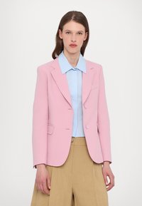Rosa taillierter Blazer mit Revers, zwei Knöpfen und Seitentaschen, getragen über einem hellblauen Hemd und beigen Hosen. Glatte Textur.
