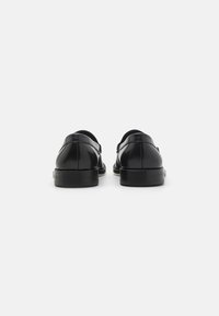 Scarpe in pelle nera con una finitura liscia, punta arrotondata e una suola nera bassa e resistente. Presentano una fascia posteriore per una vestibilità sicura.