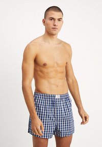 Boxers à carreaux bleu et blanc avec une ceinture élastique et une étiquette visible à l'avant, fabriqués en tissu léger.