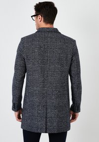 Abrigo de cuadros en navy y blanco con un corte ajustado, que presenta un cuello con muesca, mangas largas y una abertura trasera sencilla. Textura suave con puños abotonados.