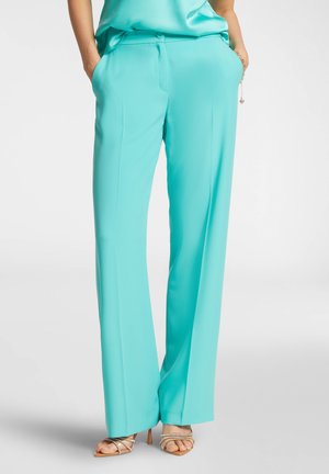 Pantaloni larghi turchesi con una texture liscia, tasche anteriori e una vita aderente. Abbinati a tacchi beige con cinturini.