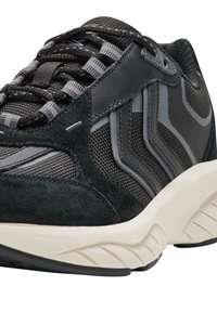 Mustavalkoinen ja harmaa urheilukenkä, jossa on mokka- ja verkkokangas-sekoitus, teksturoitu pohja ja näyttävät käyrät korostukset sivuilla.