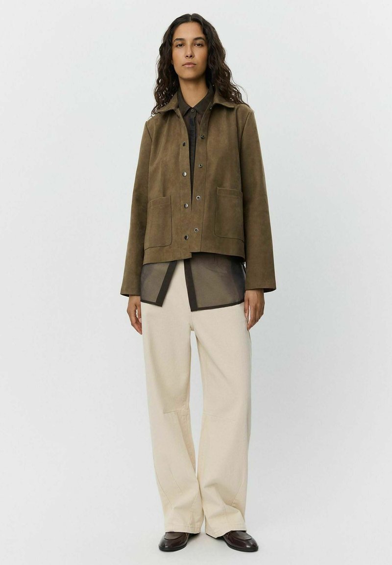 Bruine suedjacket met een kraag, snap-sluitingen en voorzakken, gedragen over een gelaagd donkere top en beige wijde broek.